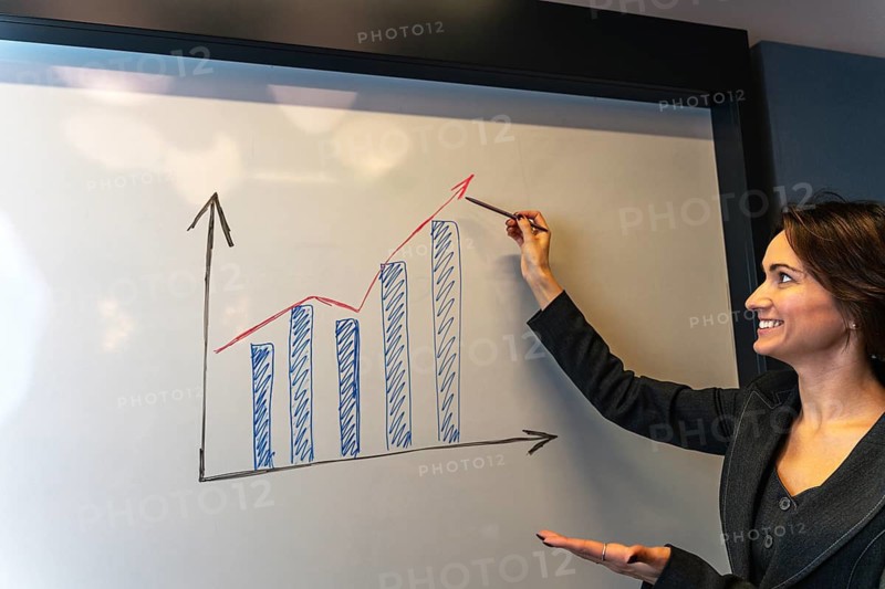 Successful businesswoman presenting growth results with open gesture at whiteboard