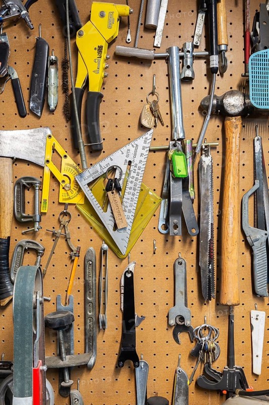 Various hand tools including axe, hammer, clamps, metal saw blades, keys hanging on light brown colored pegboard wall in home garage workshop, Quebec, Canada
