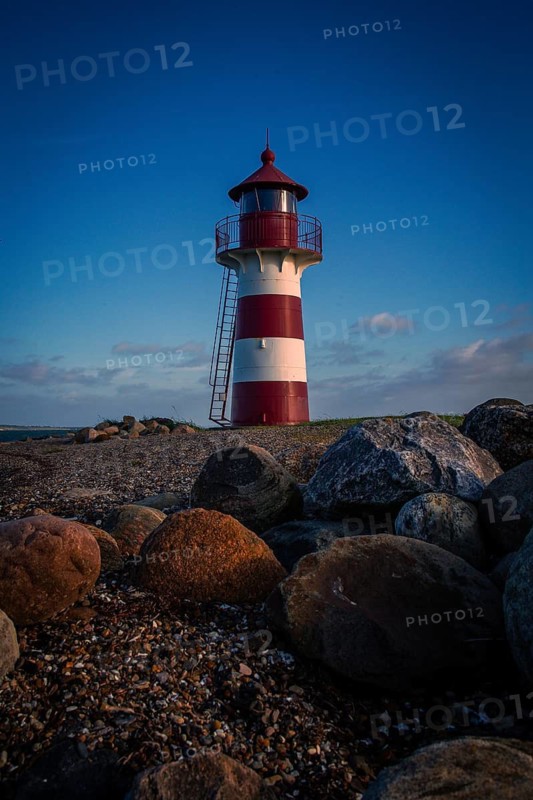 A red and white lighthouse stands on a rocky beach in the evening mood in calm skies, Grisetaodde lighthouse, Neno Sound in the Limfjord, North Jutland, Denmark