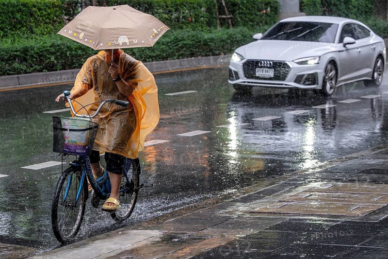 Female cyclist and passenger car in rain, Bangkok, Thailand