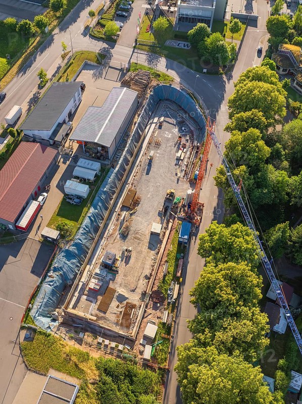 Construction site in advanced construction phase, surrounded by trees and vehicles on a neighboring road, Parkhaus Bau, Calw, Germany