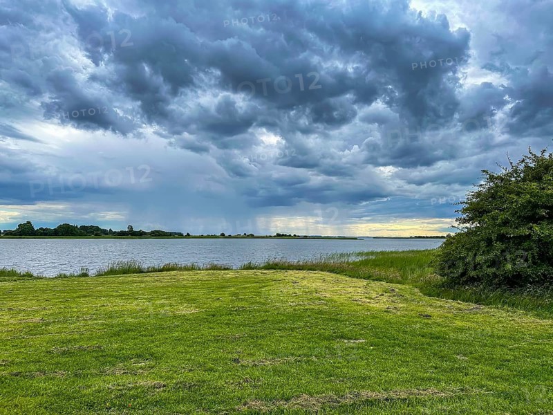 A vast landscape with cloudy sky over a lake and grassy area, Ummanz, Mecklenburg-Western Pomerania, Germany