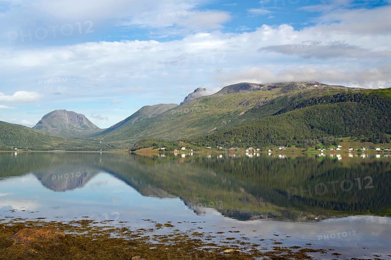 A calm lake with reflections of the mountains and the sky. Small settlement in the background, Botnhamm, Troms, Senja, Norway