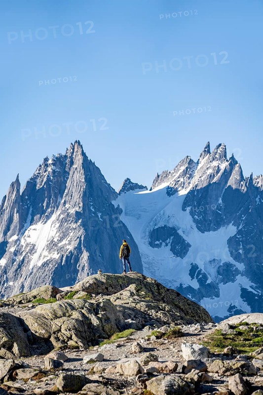 Young man in front of impressive mountain landscape in morning light, reflection in the Lac Blanc mountain lake, mountain summit, Aiguille Verte, Grandes Jorasses, Aiguille du Moine, Mont Blanc, Mont Blanc Massif, Chamonix-Mont-Blanc, Haute-Savoie, France