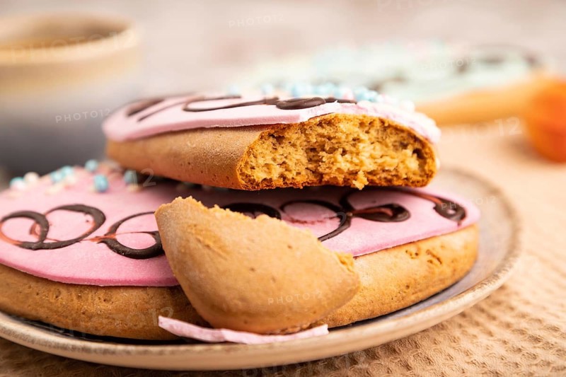 Glazed pink and blue decorated cookies, cup of coffee, on brown concrete background with linen beige textile, close up, side view, selective focus