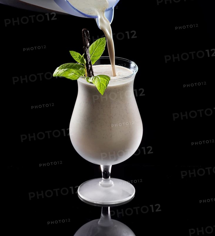 Light brown cocktail is poured against a black background, mint and vanilla bean as garnish, studio recording
