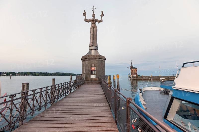 Wooden pier leading to the Imperia statue with the historic gauge house and a passenger ship in Constance, Baden-Wuerttemberg, Germany