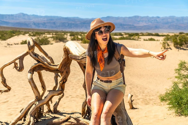 Woman traveler sitting on driftwood and pointing in the desert, experiencing adventure and exploration in the vast landscape of death valley national park