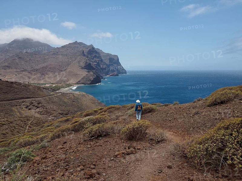 Female hiker on a hiking trail along the coast with views of sea and mountains, La Aldea de San Nicolas, Gran Canaria, Spain