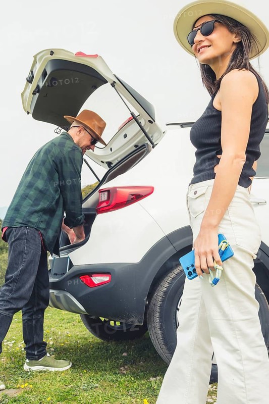 Excited Traveling couple packs puts big luggage to white rented SUV vehicle trunk on scenic Mediterranean viewpoint. Weekend get away road trip arrival, travel preparation, planning holiday excitement
