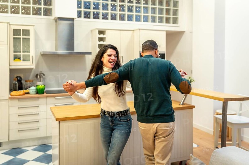 Cheerful couple dancing and embracing in their modern white kitchen, sharing a lighthearted, romantic moment of joy, laughter and togetherness at home