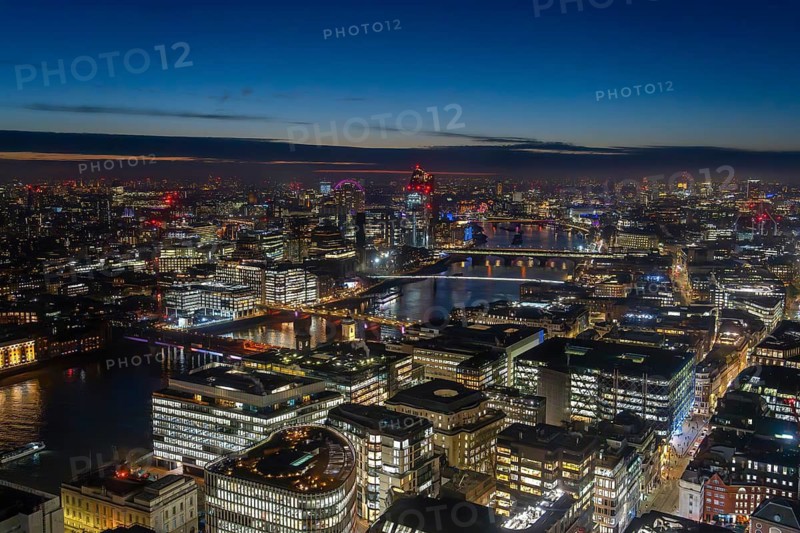 Aerial view over the River Thames and skyline showing illuminated skyscrapers and highrise buildings in the capital city London at sunset, England, UK