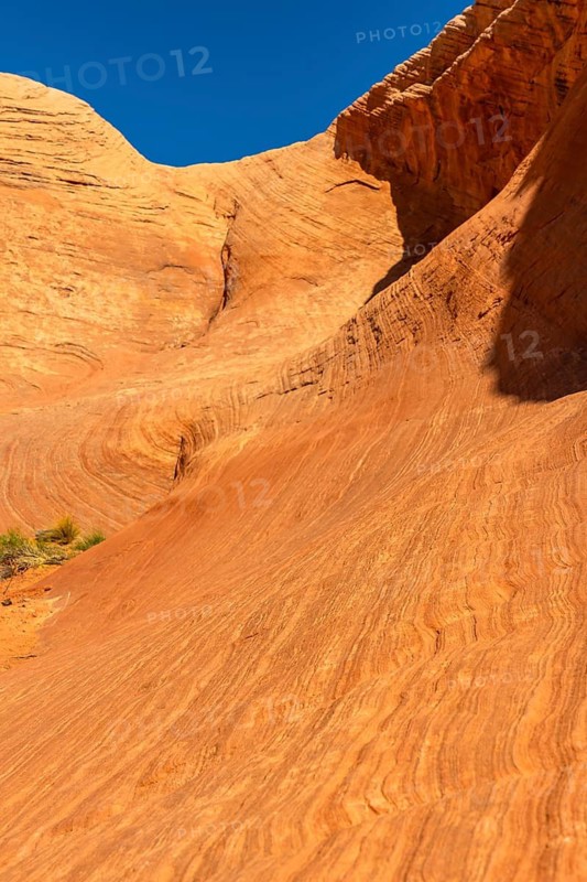 Biidi the arch cave in page, arizona revealing an abstract pattern of orange and red sandstone layers sculpted by wind and water erosion under a clear blue sky