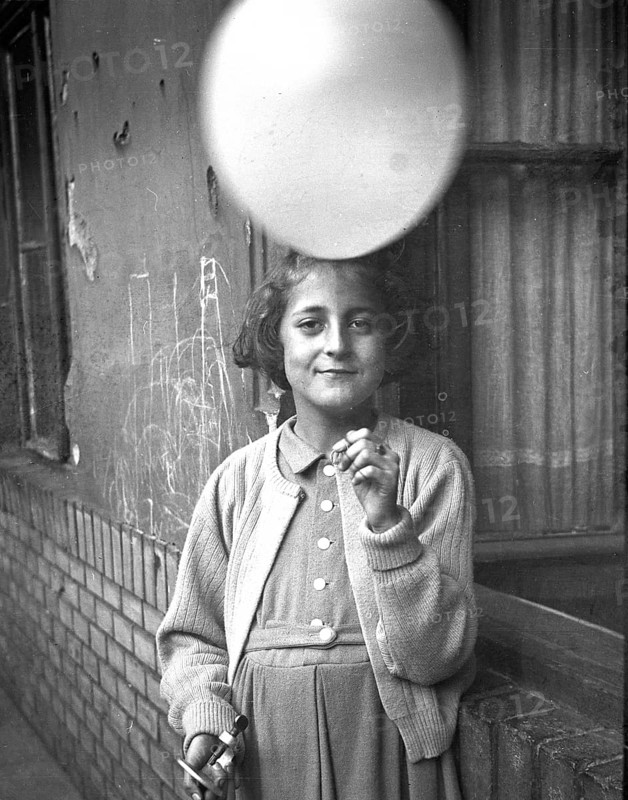 Girl, balloon, happiness, satisfaction, gift, smile, grace, twenties, a child holding a balloon and smiling in front of a wall dressed in period clothing, around 1926