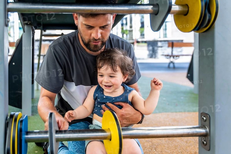 Father and young son playing together on colorful playground equipment, sharing a happy moment outdoors and enjoying family time with a joyful expression