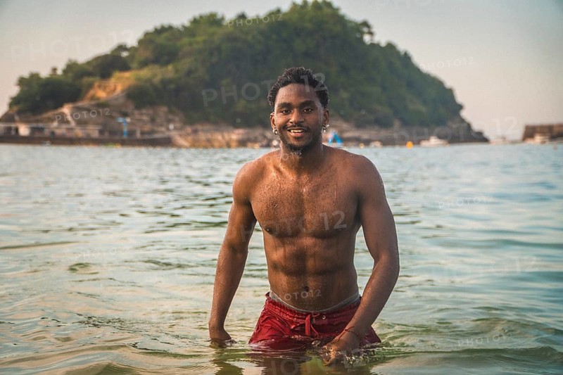 Young man smiling at camera while swimming in the ocean on a summer vacation, with an island in the background, representing health, fitness, and relaxation
