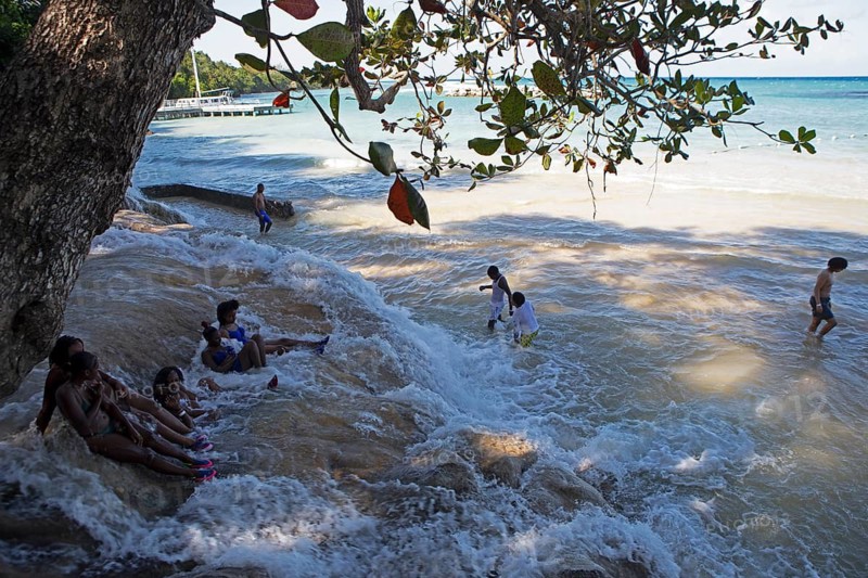 Jamaican woman sit on rocks at Dunn's River Falls or waterfalls at the mouth of the Caribbean Sea, Ochos Rios, Saint Ann Parish, West Indies, Caribbean, Central America