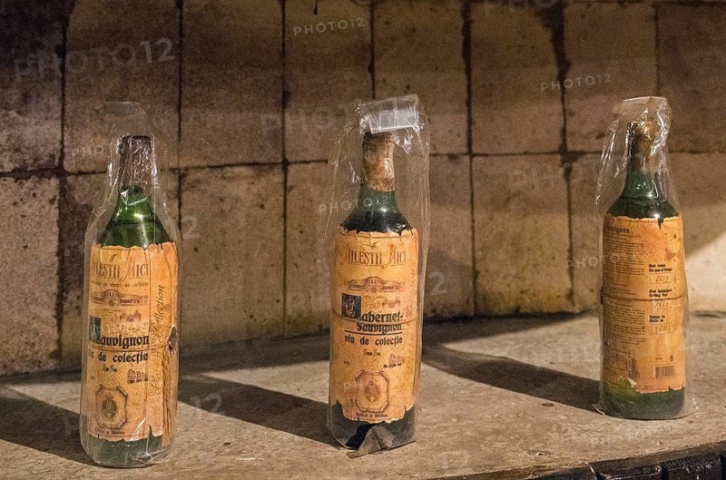Three old wine bottles with labels and protective film in a historic cellar environment under light and shadow, wine cellar, Milestii Mici winery, Mile?tii Mici, Republic of Moldova, Moldova