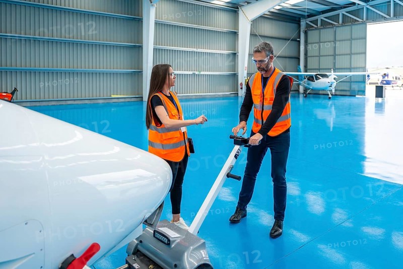 Aviation engineers collaborating, moving a small airplane using an aircraft tug in a clean hangar, representing teamwork, logistics, maintenance, and safety in aviation operations