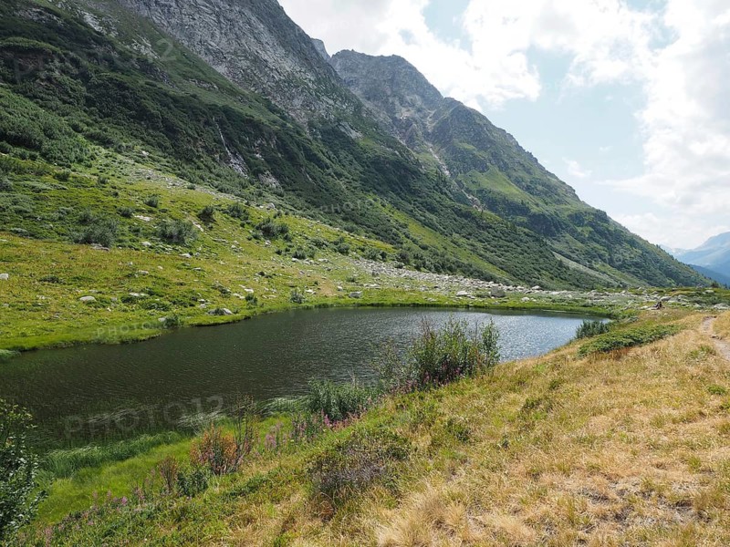 Small mountain lake, Halsesee, surrounded by green meadows and steep cliffs, Binntal Landscape Park, Goms, Canton of Valais, Switzerland