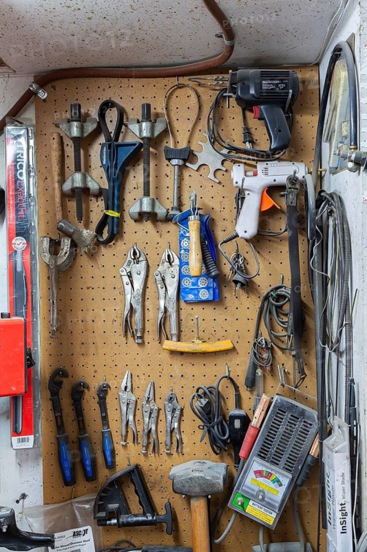 Various hand tools including vise grips, soldering and glue guns, sledge hammers hanging on light brown colored pegboard wall in home garage workshop, Quebec, Canada