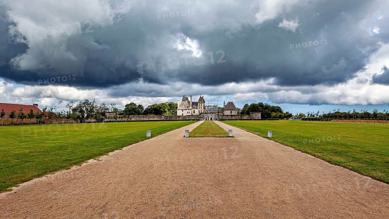 A castle in the distance with dramatic skies and dark clouds surrounded by lawns, Château de Kerjean Castle in Brittany