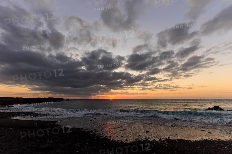 Lanzarote, Canary Islands, Spain, Europe, Los Hervideros, An almost hidden sunset with clouds and a calm sea that sends waves to the beach