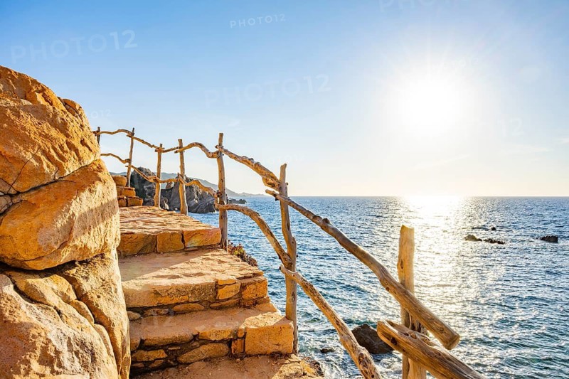 A little trail passing the rocks at the coastline with blue water at Costa Paradiso on a sunny day at sunset, Sardinia, Italy