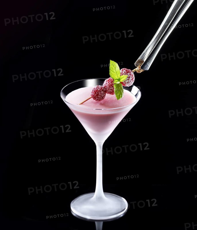 Red cocktail in iced glass against a black background, mint and raspberry skewer as garnish, studio shot