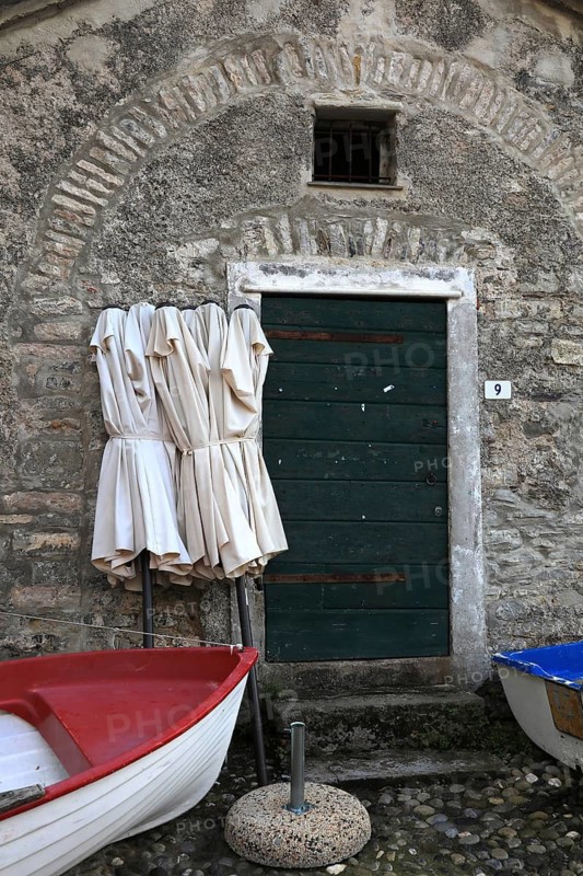 Rest in pre-season, folded umbrellas and a fishing boat ashore in front of a building. Tellaro, village in the municipality of Lerici and belongs to the association I borghi piu belli d'Italia, The Most Beautiful Towns in Italy, Province of La Spezia, Liguria, Italy