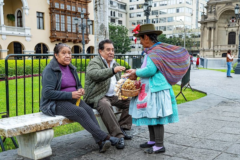 Street scene, an elderly woman in traditional clothing from the Quechua indigenous population offers fruit for sale to an elderly couple, Plaza de Armas, main square, Lima, Peru, South America
