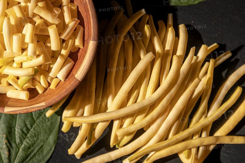 Whole and sliced yellow beans in a wooden bowl and on a dark background