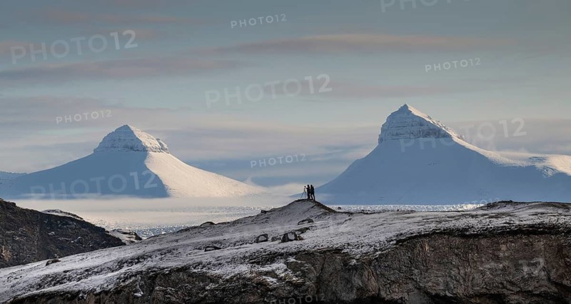 Two people, including a photographer with a stand in front of two of the three mountains Tee Kroner, Kongsfjord or Kongsfjorden, Spitsbergen archipelago, Svalbard, Norway