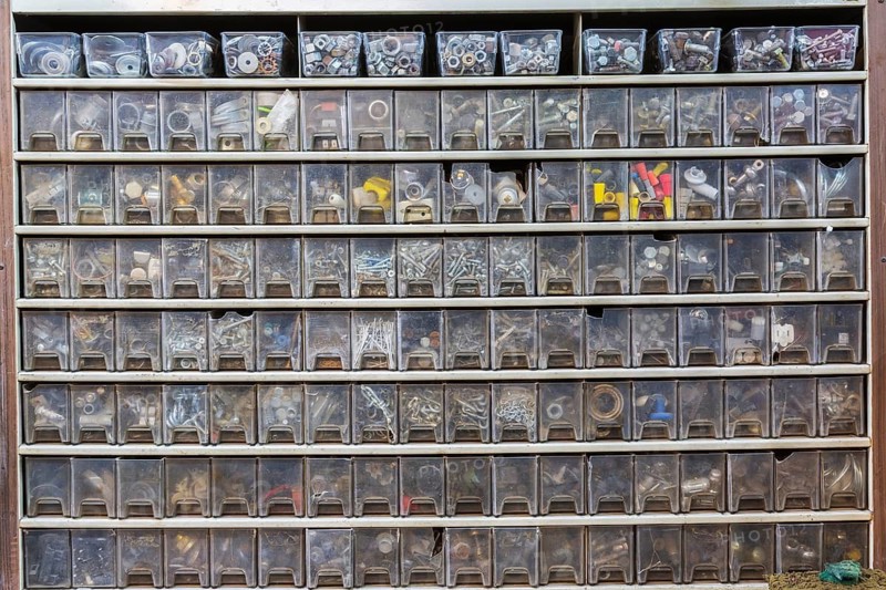 Cabinet with rows of plastic parts drawers showing washers, nuts screws, wire connecting caps in home garage workshop, Quebec, Canada
