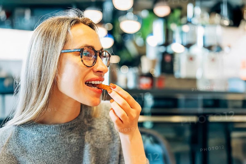 Smiling woman with glasses enjoying a crispy snack in a modern cafe
