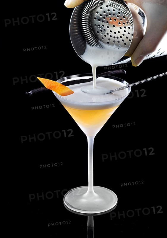 Orange-colored cocktail is filled with cream, against a black background, orange peel and vanilla bean as a garnish, studio shot
