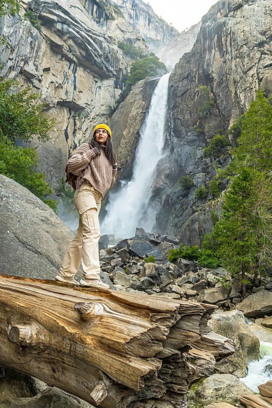 Woman stands on a fallen log, surveying lower yosemite falls and surrounding mountains, forests, and stream hiker enjoying peaceful wilderness view and discovery