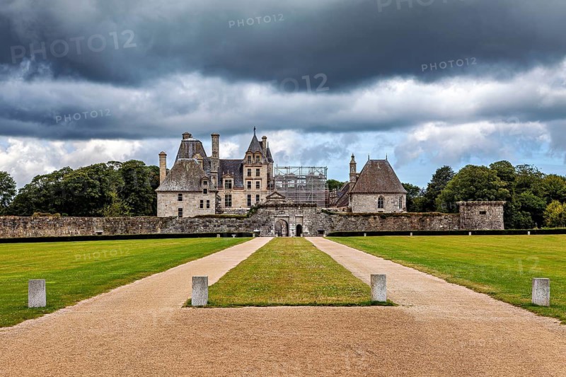 A large castle with a straight gravel path, dramatically illuminated by dark clouds, The Château de Kerjean Castle in Brittany