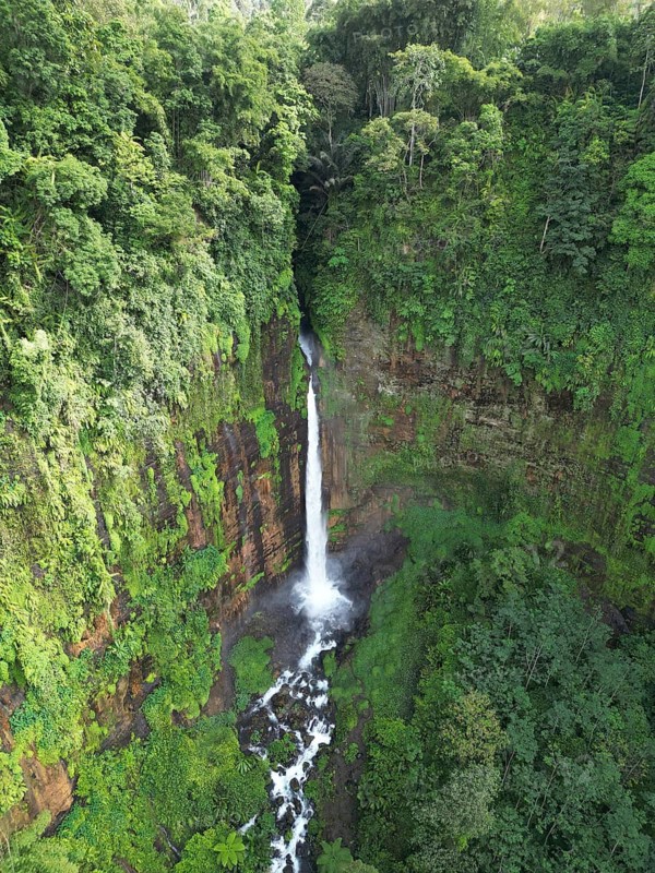 An impressive waterfall plunges into the depths amid thick tropical vegetation, surrounded by lush greenery and steep rocks, Kapas Biru Waterfall, Jakarta, Indonesia, East Java's