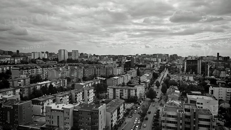 Black and white cityscape with densely packed buildings under a dramatically cloudy sky, Pristina, Kosovo