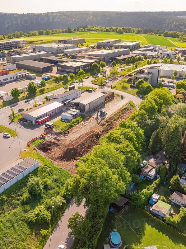 Aerial view of an industrial area with construction site surrounded by green spaces and buildings in sunny weather, Parkhaus Bau, Calw, Germany