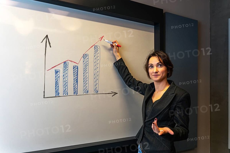 Businesswoman presenting growth chart with questioning gesture at whiteboard meeting