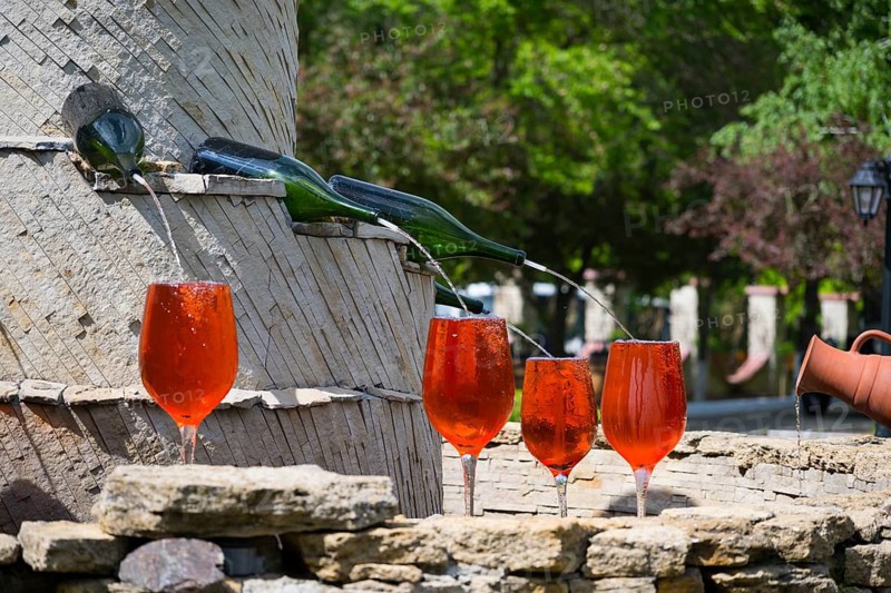 Red glasses under a wine fountain, flowing from bottles across stone, in sunshine, fountain with wine bottles filling glasses, Milestii Mici Winery, Mile?tii Mici, Republic of Moldova, Moldova