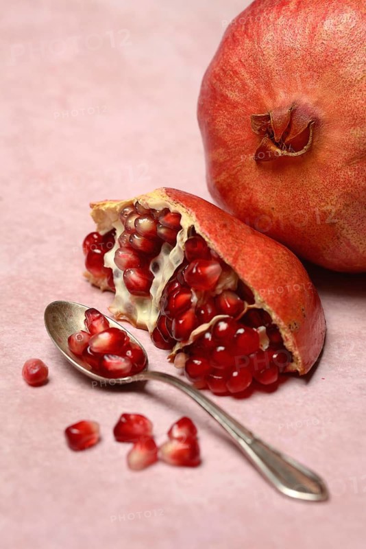 Opened pomegranate and pomegranate seeds in a spoon, Punica granatum