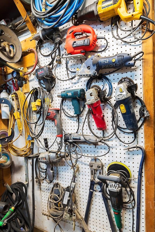 Various electric power tools including drills, circular sanders, jig saw hanging on white pegboard in home garage workshop, Quebec, Canada