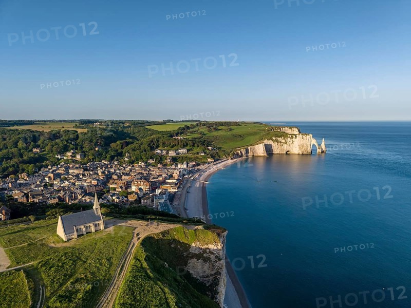 Aerial view of the Notre Dame de la Garde chapel after sunrise at the Falaise d'Amont viewpoint, on the right the coastal town of Étretat with the beach, on the horizon the Porte d'Aval rock formation, Étretat, Alabaster Coast, La Côte d'Albâtre, chalk cliffs, English Channel, Seine-Maritime, Normandy, France