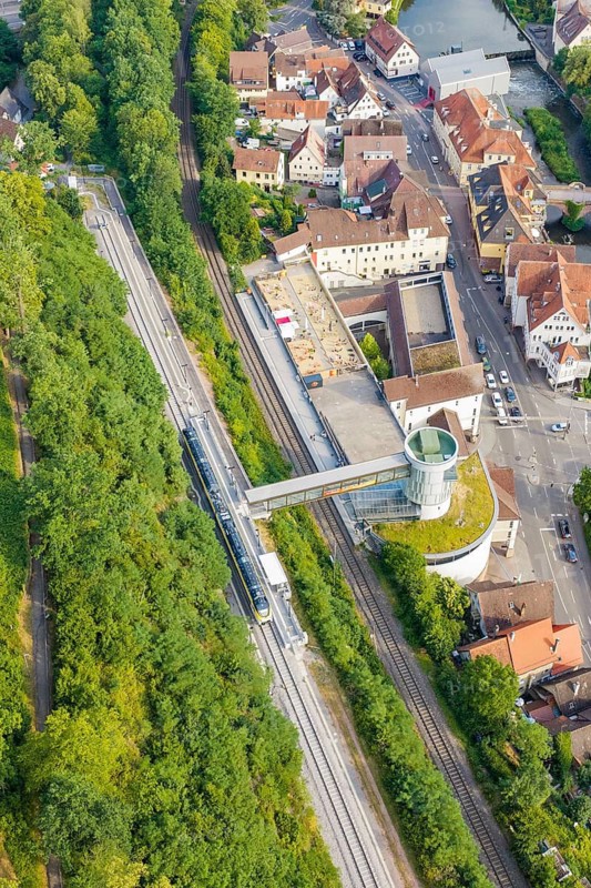 Train crosses bridge, urban environment with dense greenery and building structures, Hermann Hesse Railway, Calw, Germany