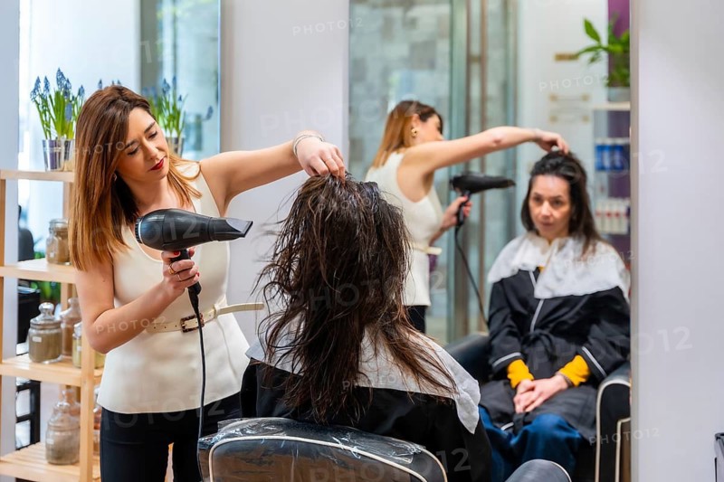 Professional hairdresser blow drying and styling a female client in a modern salon, focusing on grooming, beauty care and expert technique during a pampering appointment