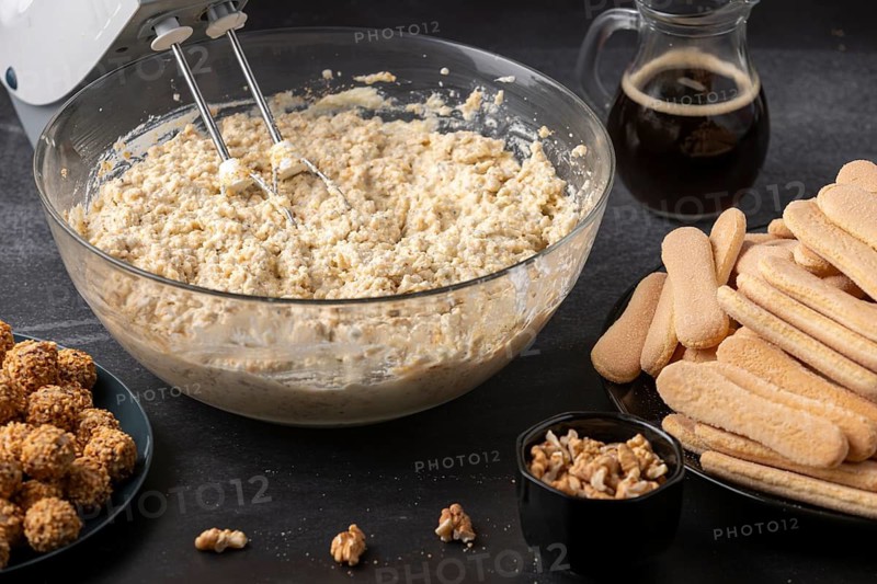 Curd cream is stirred in a glass bowl, followed by sponge cake, coffee and nuts
