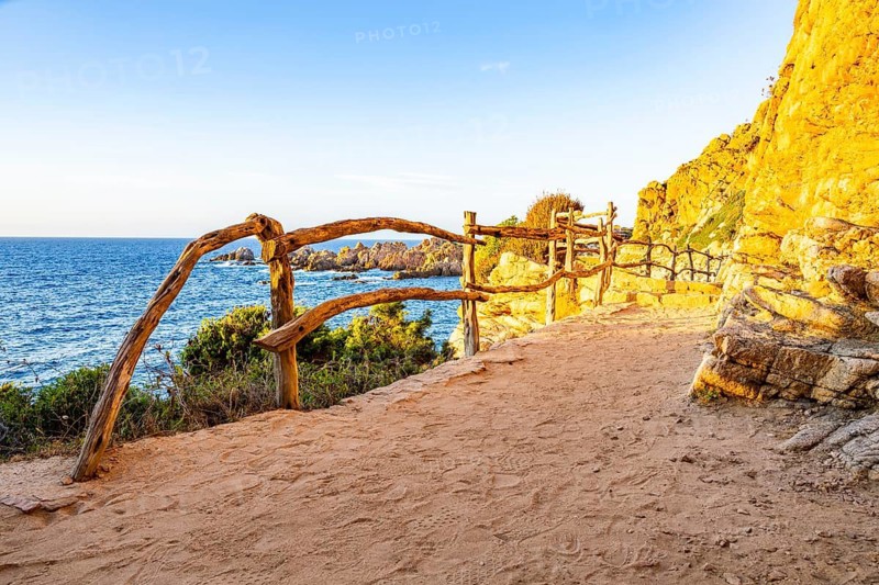 A little trail passing the rocks at the coastline with blue water at Costa Paradiso on a sunny day at sunset, Sardinia, Italy